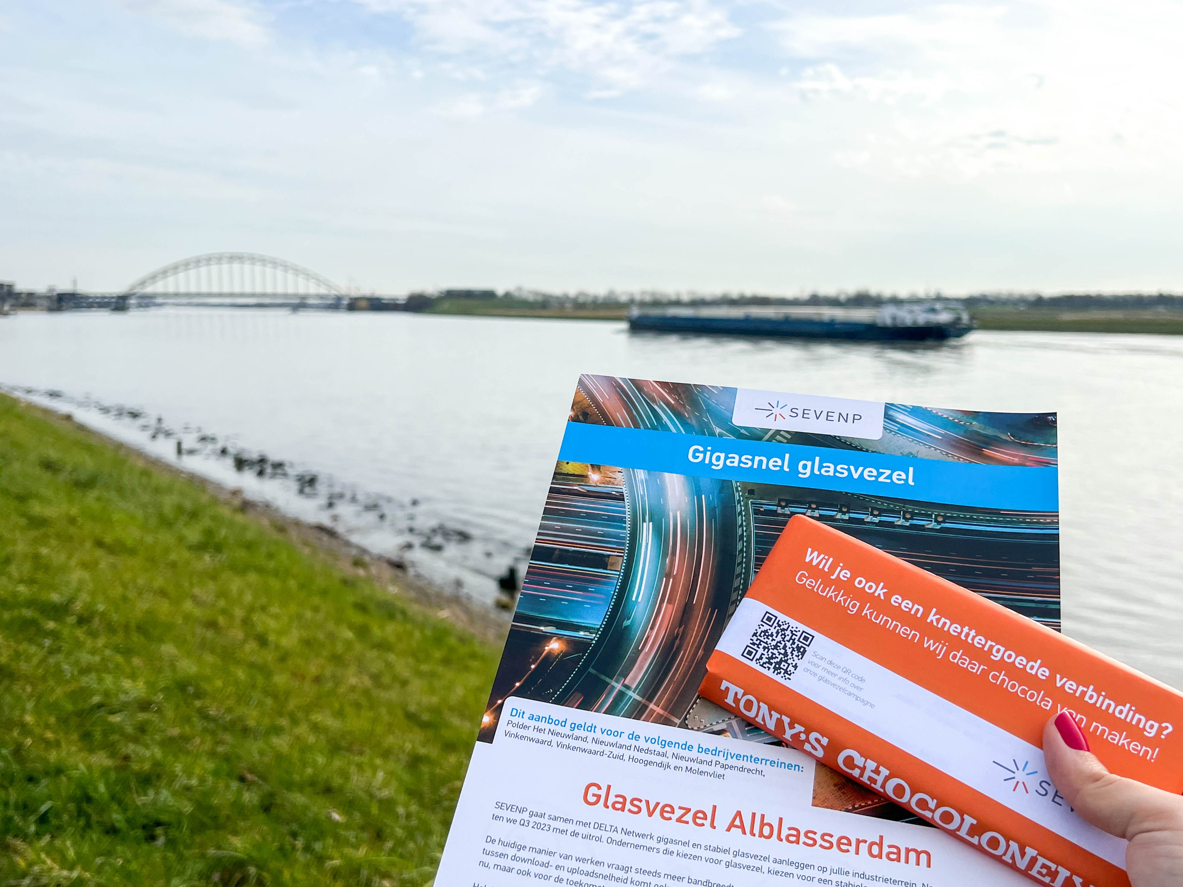 Foto met flyer en chocoladereep van de glasvezelcampagne van SEVENP. Met als achtergrond de brug over de Noord bij Alblasserdam.